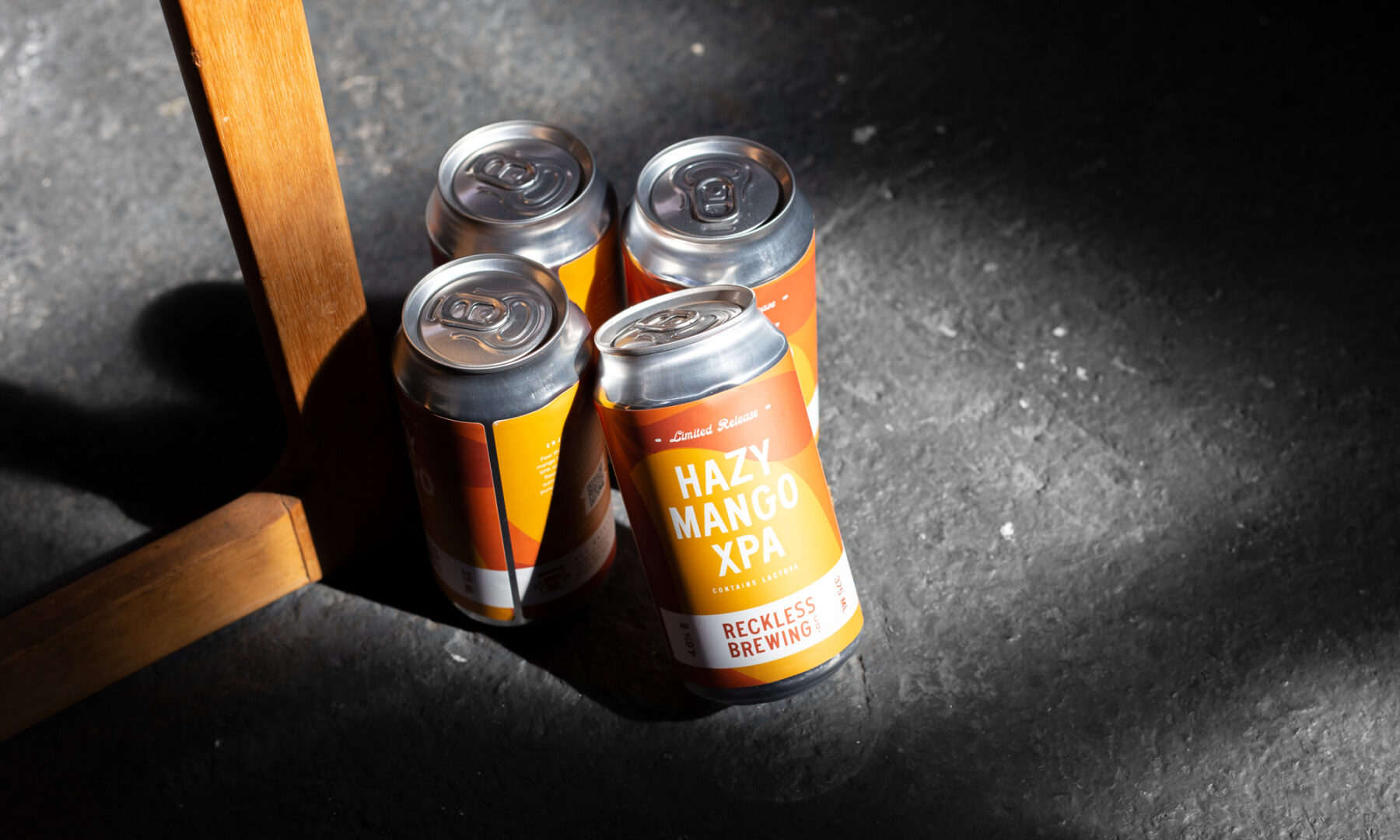 4 Reckless Brewing Hazy Mango XPA cans on industrial background